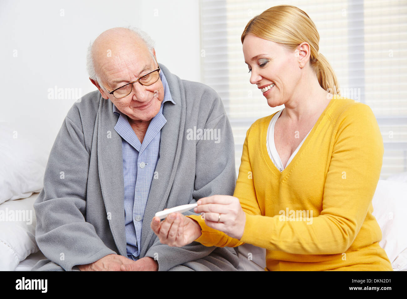 Lächelnde Frau, die die Temperatur des älteren Mannes mit thermometer Stockfoto