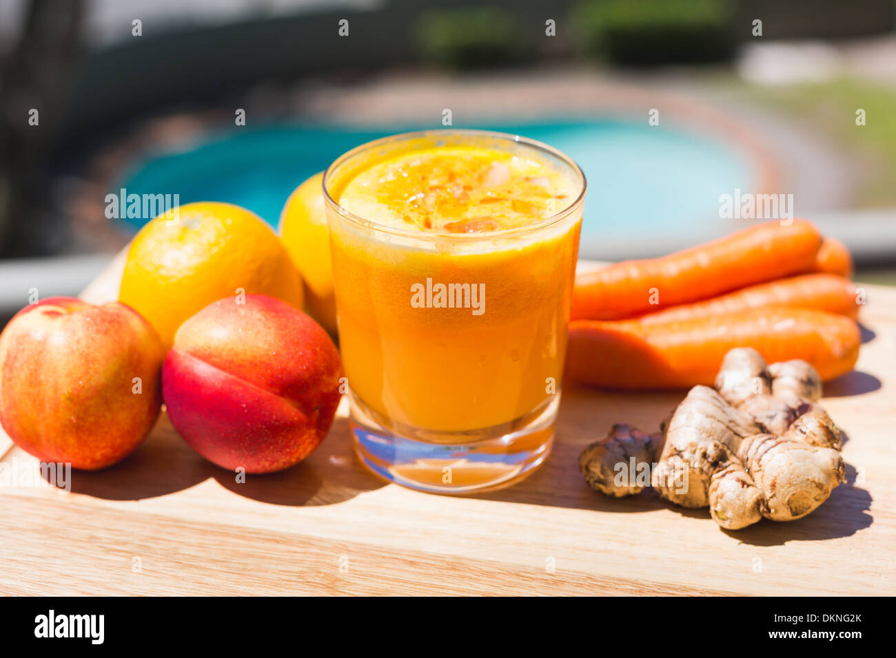 Obst, Gemüse und Orange Glas Saft im Außenbereich mit Pool im Hintergrund Stockfoto