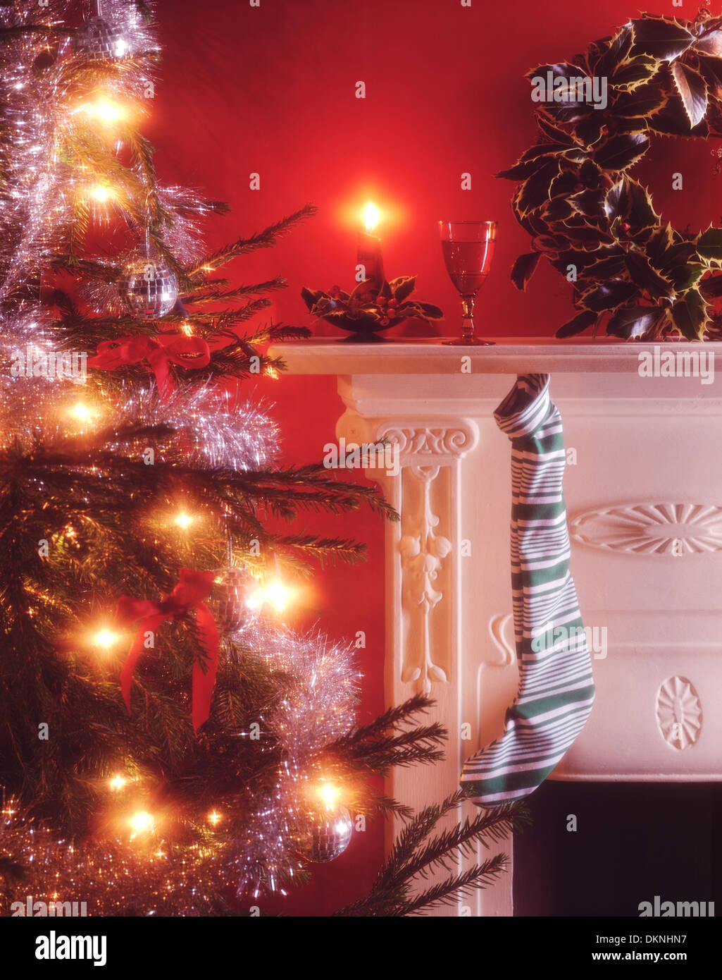 Weihnachten eines Kindes Strumpf auflegen auf einem kaminsims Neben einem geschmückten Weihnachtsbaum mit Kerzenlicht und ein Glas Sherry für Santa Claus. Stockfoto