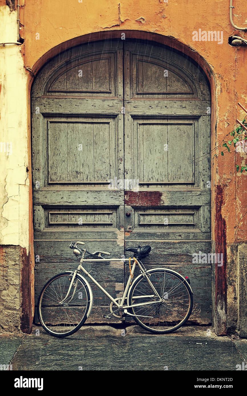 Vertikal ausgerichtete Bild Fahrrad gelehnt alte Holztür am Eingang zum Haus an regnerischen Tag in Alba, Italien. Stockfoto