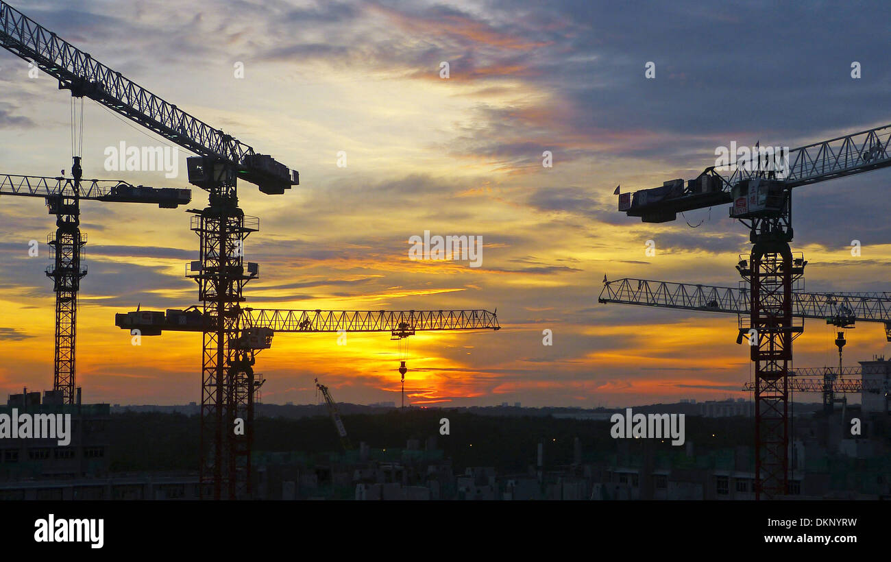 Eine Silhouette der Skyline Singapurs bei Sonnenuntergang mit Kränen und schwerer Ausrüstung auf einer Baustelle. Die Szene fängt die lebendigen Farben des Himmels und die architektonische Entwicklung dieser modernen Stadt ein. Stockfoto
