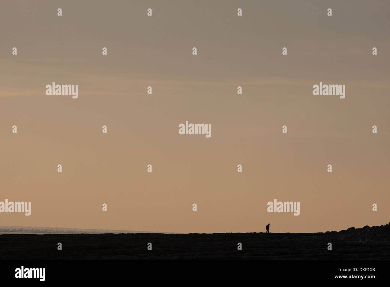 Entfernte kleine einsame Gestalt am Strand zu Fuß in der Abenddämmerung Stockfoto