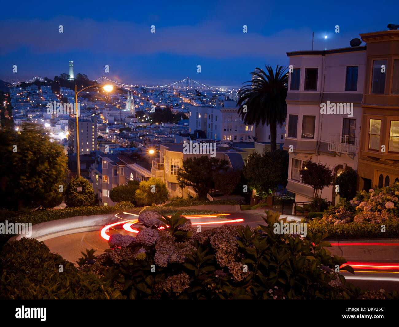 Eine Nachtansicht blickte Lombard Street in San Francisco.  Coit Tower und der Bay Bridge sind in der Ferne. Stockfoto