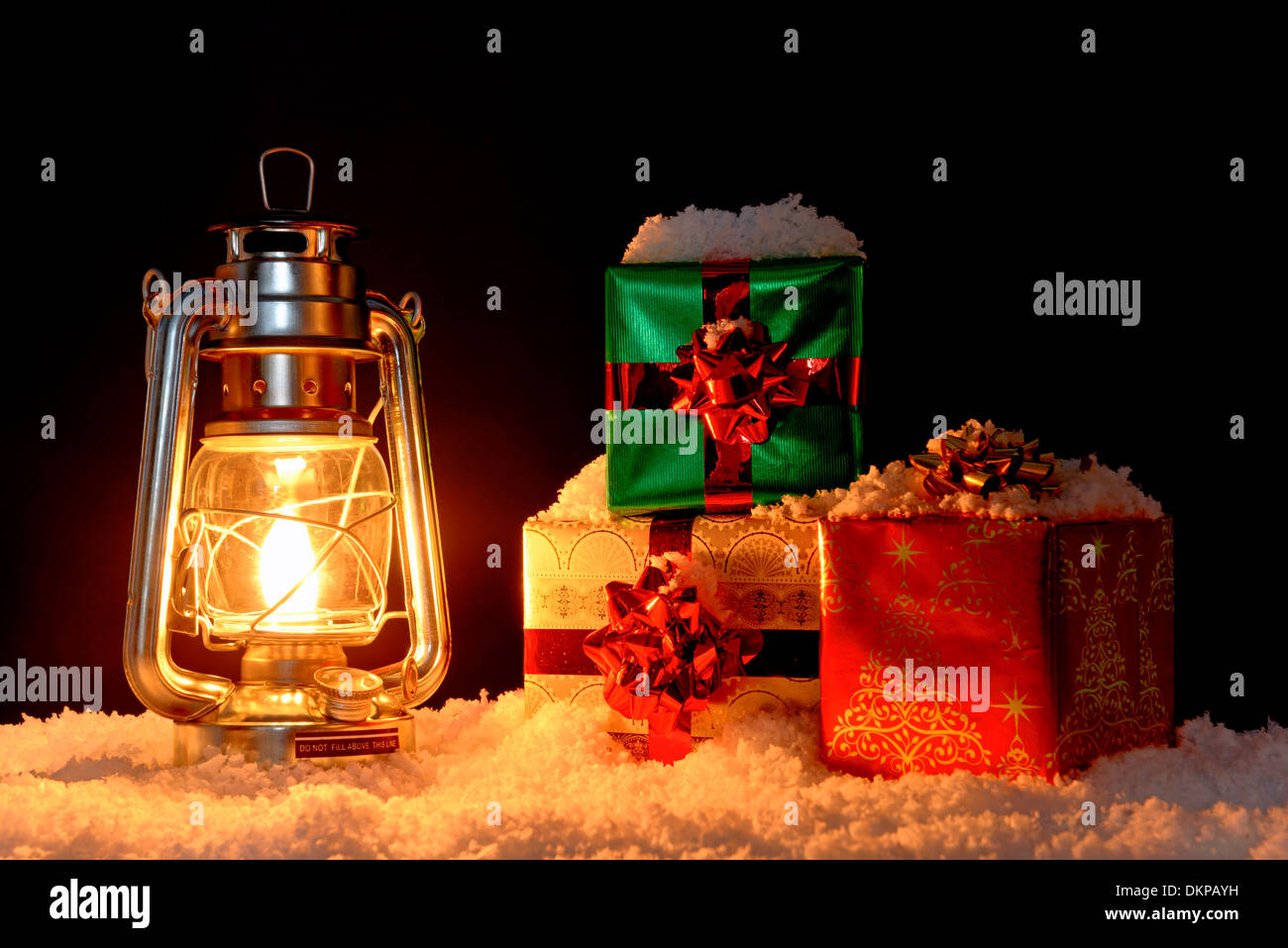 Geschenk verpackt Weihnachtsgeschenke auf Schnee mit dem Schein von einem Öl-Laterne, schwarzer Hintergrund beleuchtet. Stockfoto