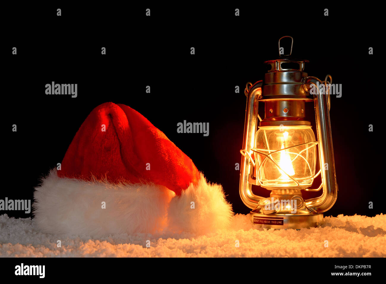 Nikolaus oder Weihnachtsmann Mütze auf Schnee, beleuchtet durch das Glühen eines Öls gefüllt Laterne, schwarzer Hintergrund. Stockfoto