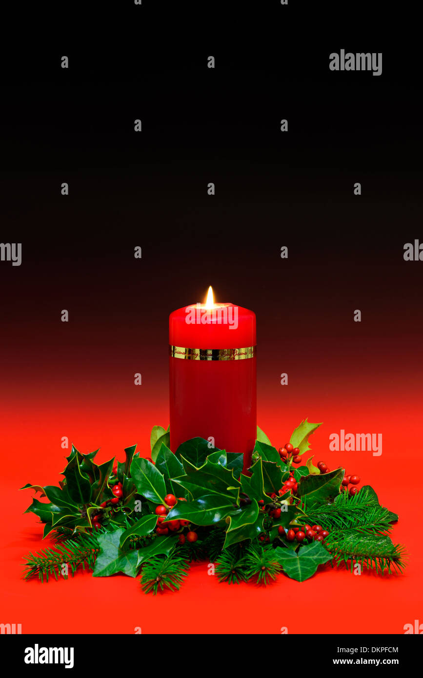 Rote Weihnachtskerze mit Holly, Efeu und Fichte auf einem roten abgestuften Hintergrund. Kopieren Sie Raum, um Ihre eigene Nachricht hinzufügen. Stockfoto