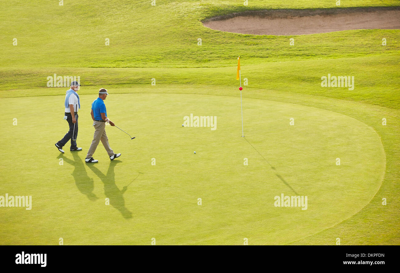 Alte Männer, die zu Fuß in Richtung Fahne und Loch am Golfplatz Stockfoto