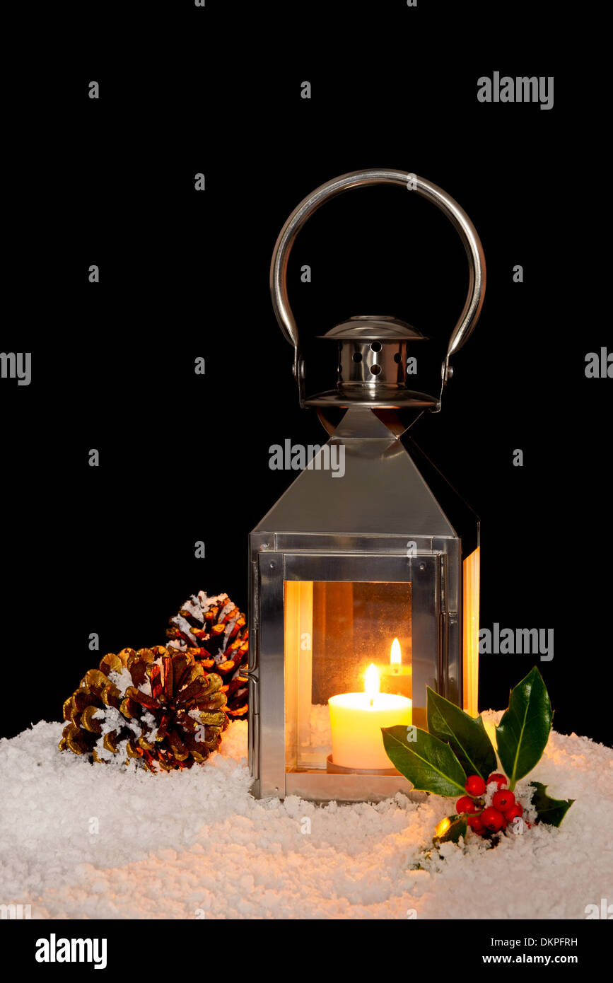 Ein Weihnachten Laterne mit einer Kerze im Schnee mit Holly und Kiefer Kegel, schwarzer Hintergrund. Stockfoto