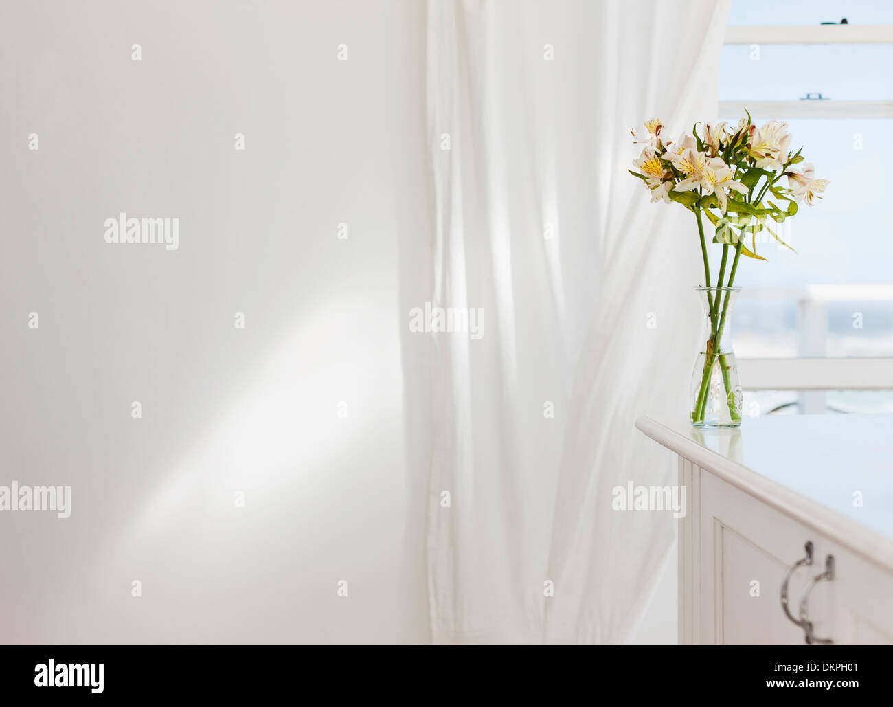 Vase mit Blumen auf Schreibtisch im weißen Raum Stockfoto