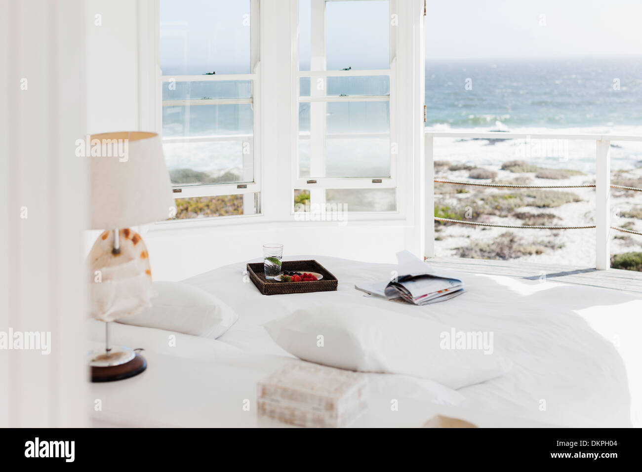 Frühstückstablett und Magazine auf Bett mit Blick auf Meer Stockfoto