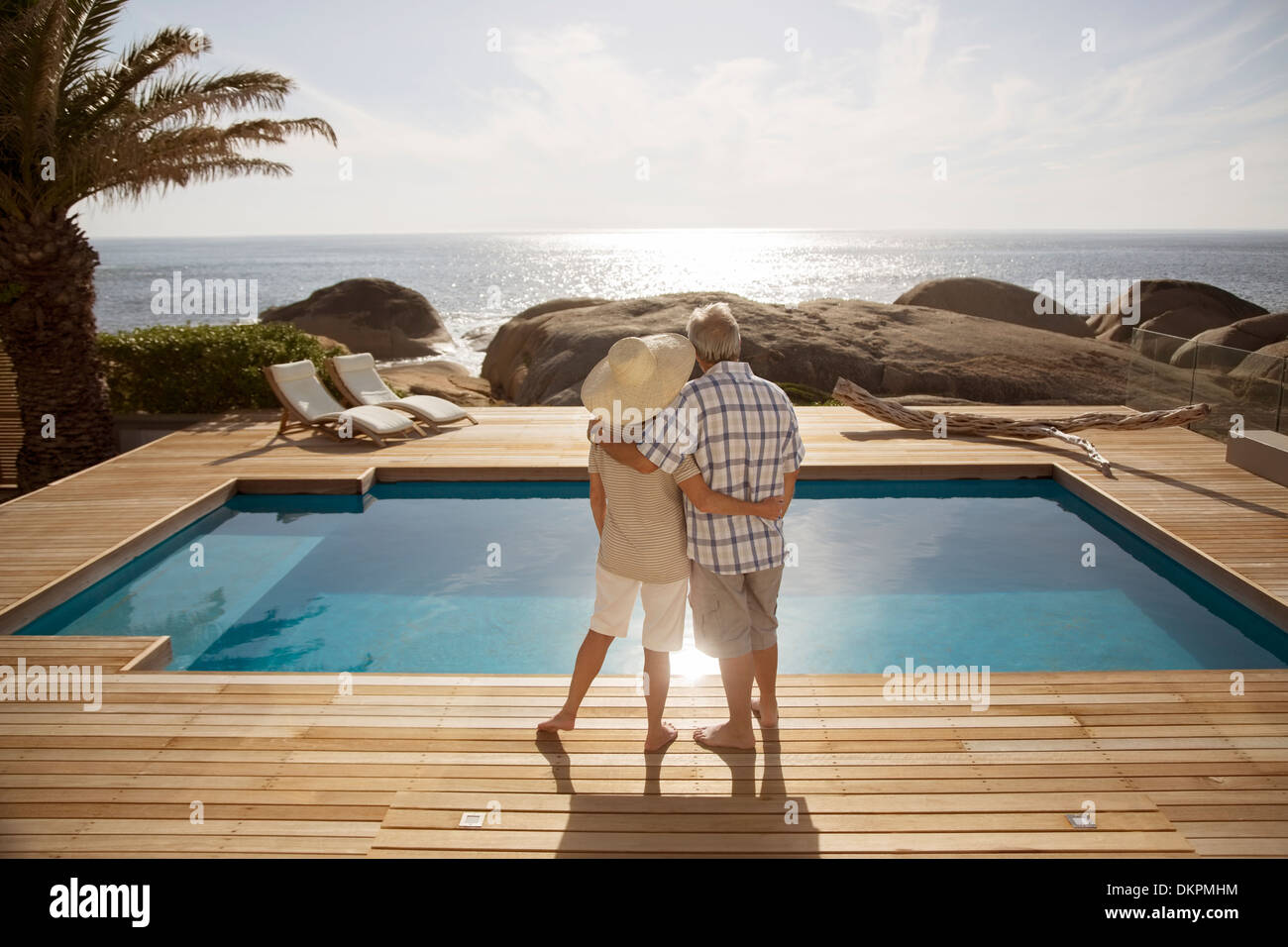 Älteres paar umarmt von modernen pool mit Blick auf Meer Stockfoto
