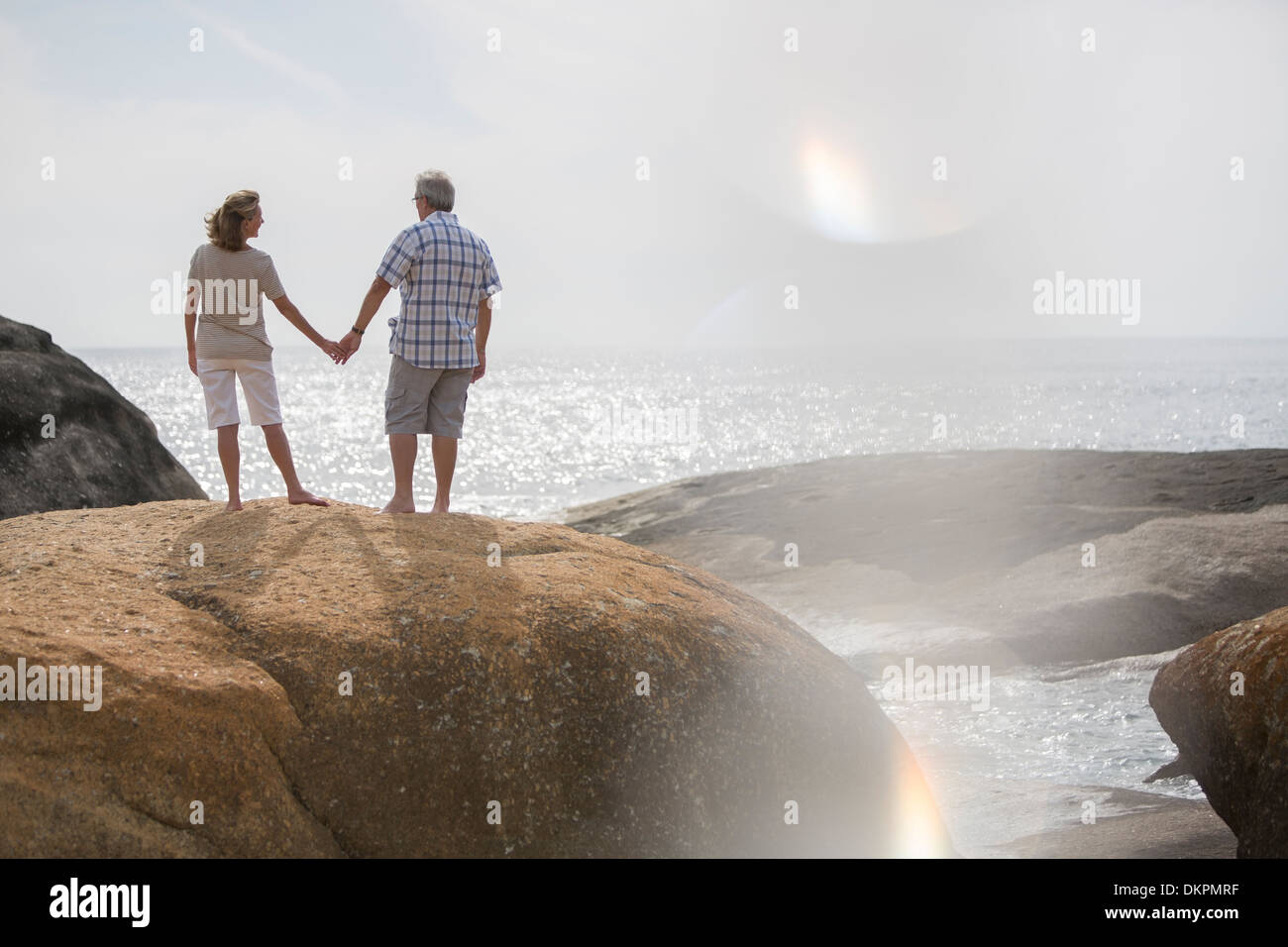 Älteres Paar halten die Hände auf Felsen am Strand Stockfoto