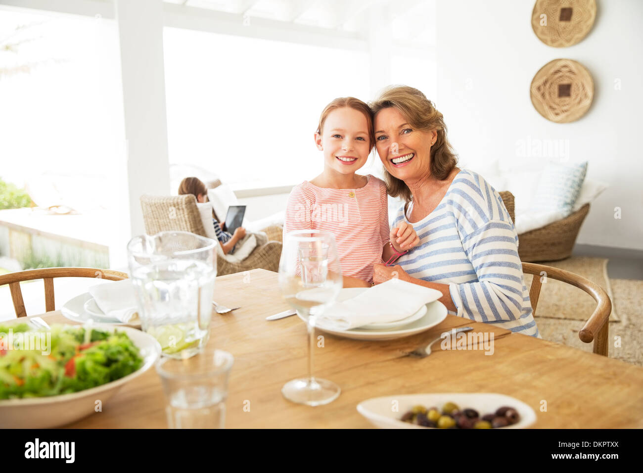 Ältere Frau und Enkelin lächelnd am Tisch Stockfoto