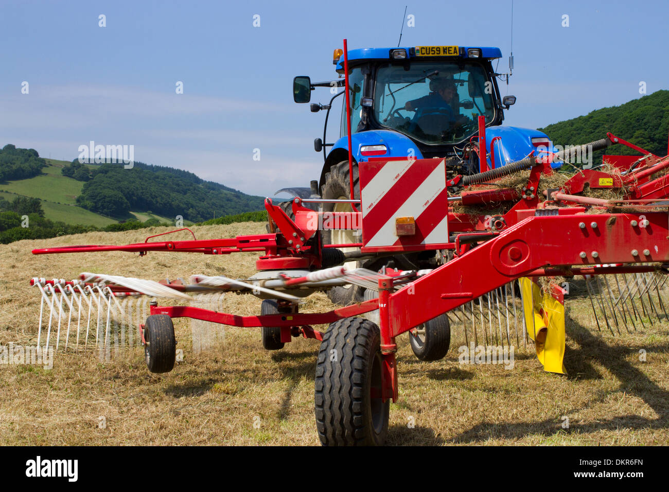 Auftragnehmer mit einem Traktor von New Holland T7030 und einen SIP-Heu-Rechen, Rechen Heu Pressen auf einem Bio-Bauernhof. Powys, Wales. Juli. Stockfoto