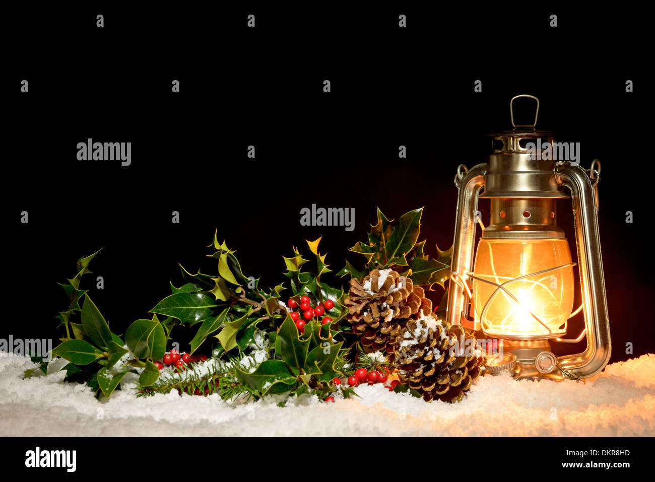 Eine ölgefüllte Laterne sitzen im Schnee mit Holly, Efeu und Kiefer Kegel durch das Leuchten der Lampe beleuchtet. Stockfoto