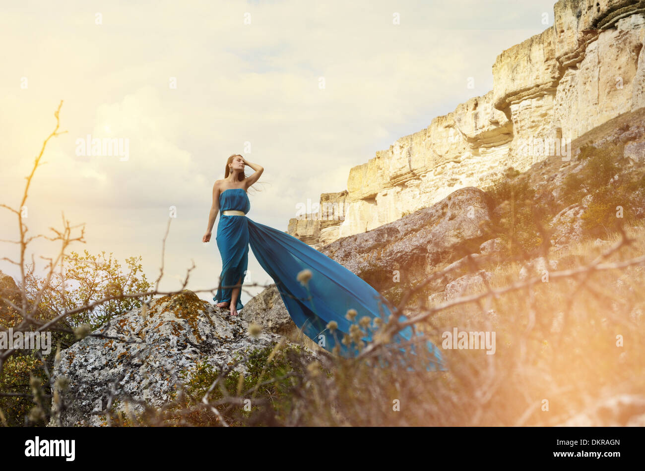 Junge schöne allein Frau im dunklen blaugrünen Kleid steht auf dem Felsen mit Bergen im Hintergrund Stockfoto