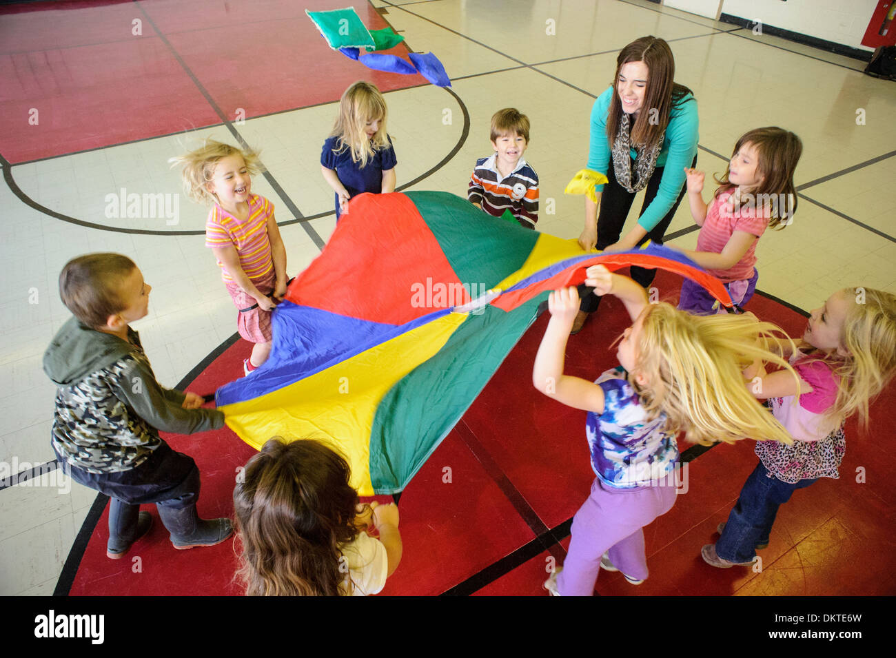 Kinder im Vorschulalter spielen mit Regenbogen Fallschirm im Fitness-Studio Stockfoto