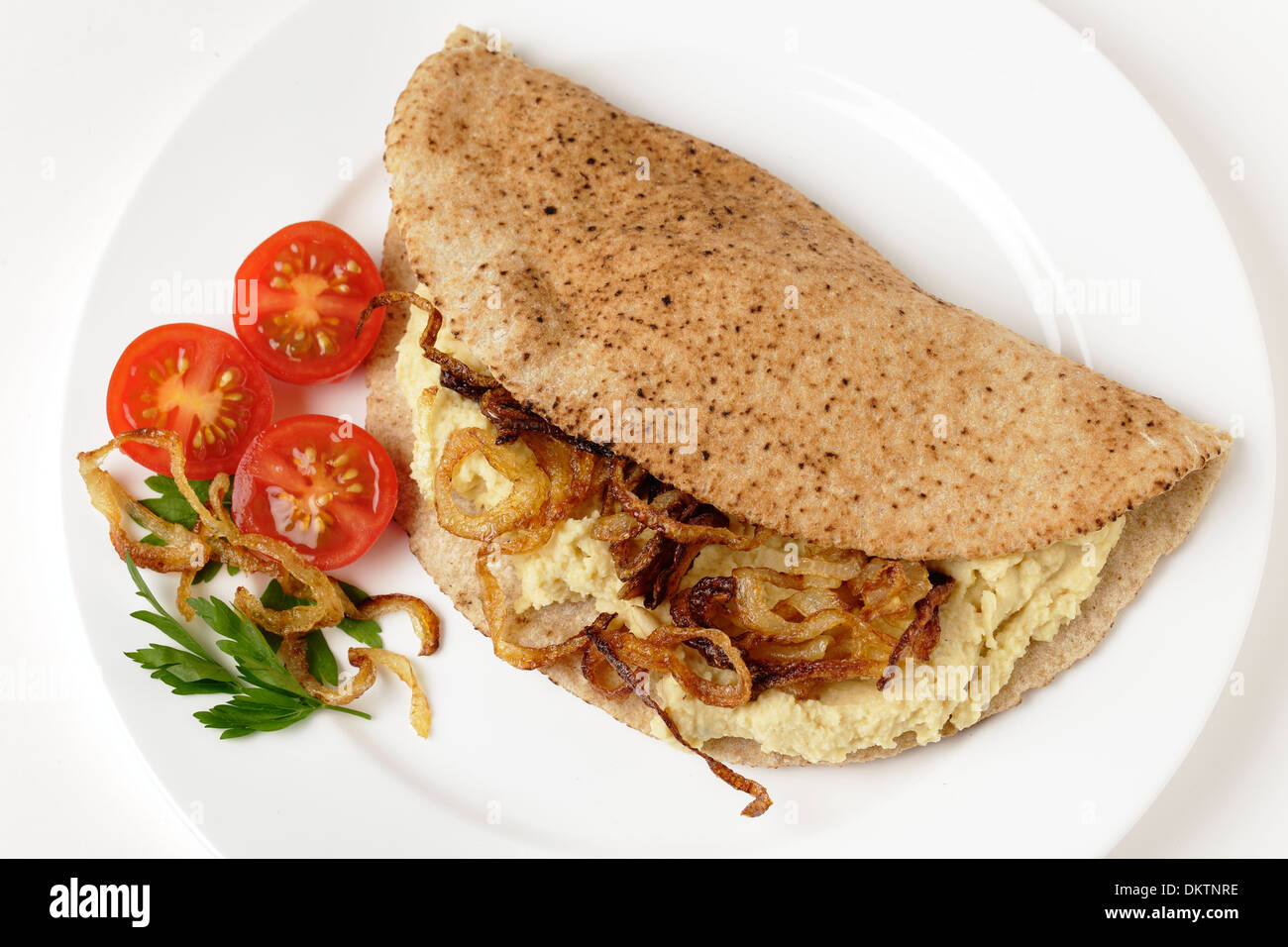 Eine Pitta-Brot, oder Kubz, Sandwich gemacht mit Hummus und karamellisierten Zwiebeln, serviert mit Tomaten und Petersilie garnieren Stockfoto