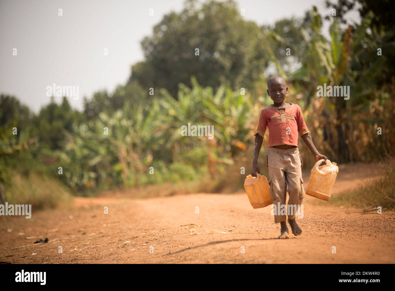 Ein Kind trägt Gießkannen in Gombe, Uganda, Ostafrika. Stockfoto