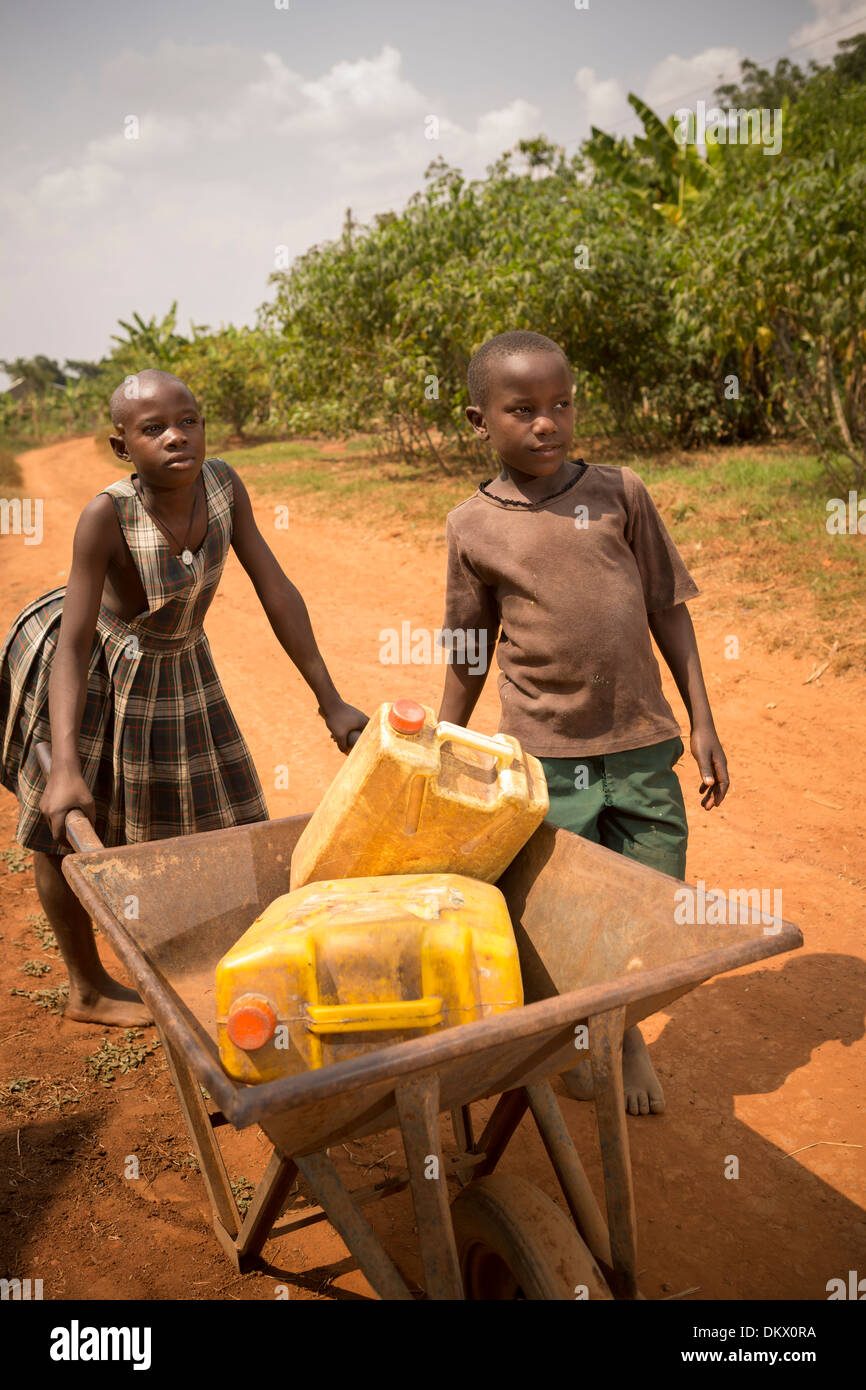 Kinder tragen Gießkannen in einer Schubkarre in Gombe, Uganda, Ostafrika. Stockfoto