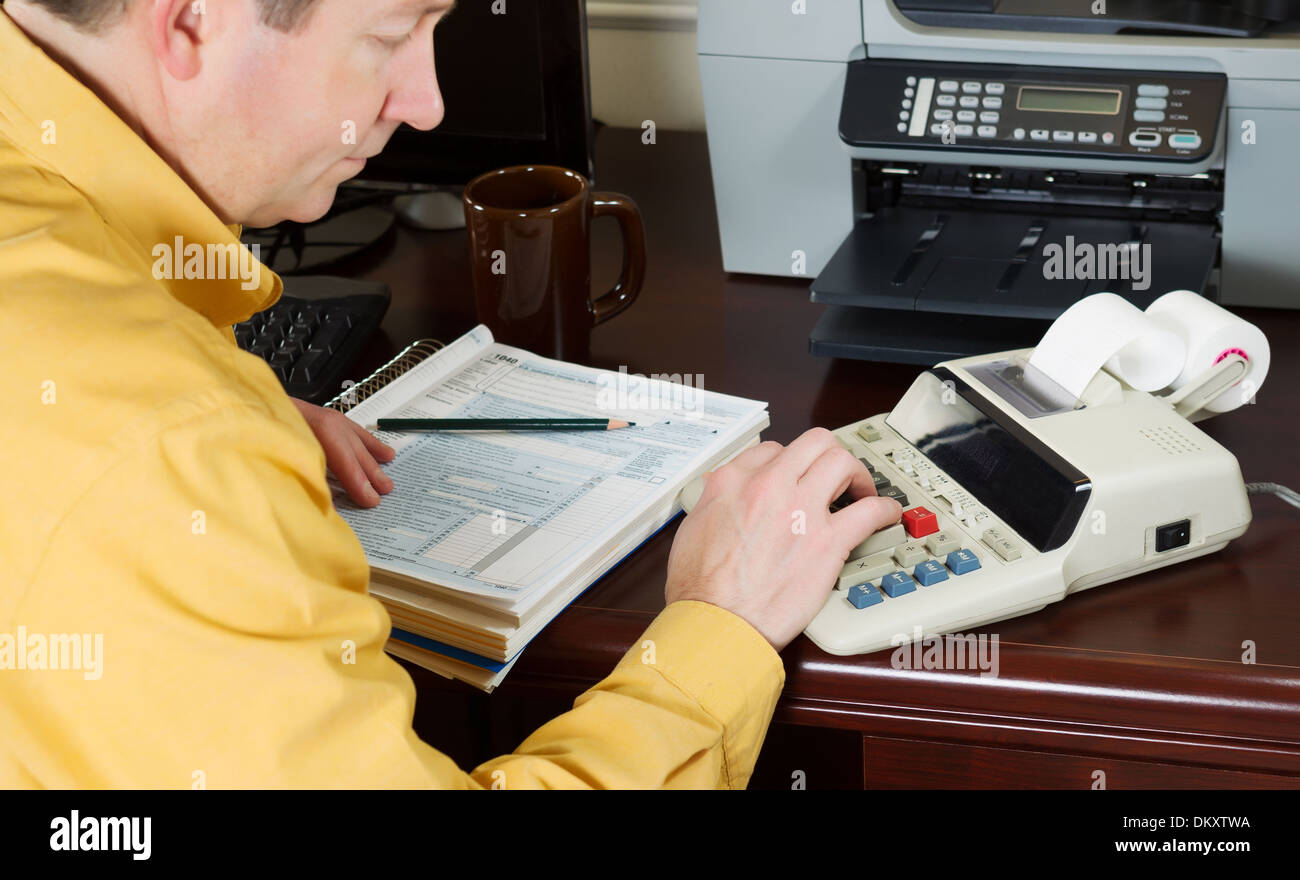 Horizontale Foto mit Fokus auf der männlichen Seite mit Taschenrechner mit Steuertabellen und andere Bürogeräte im Hintergrund Stockfoto