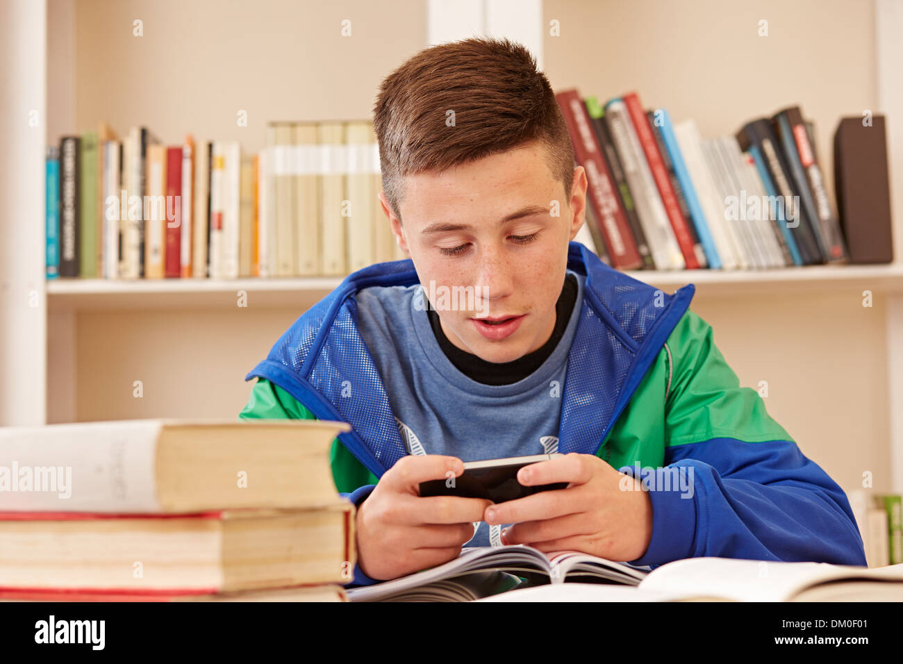 Teenager spielen oder SMS mit Smartphone während des Studiums Stockfoto