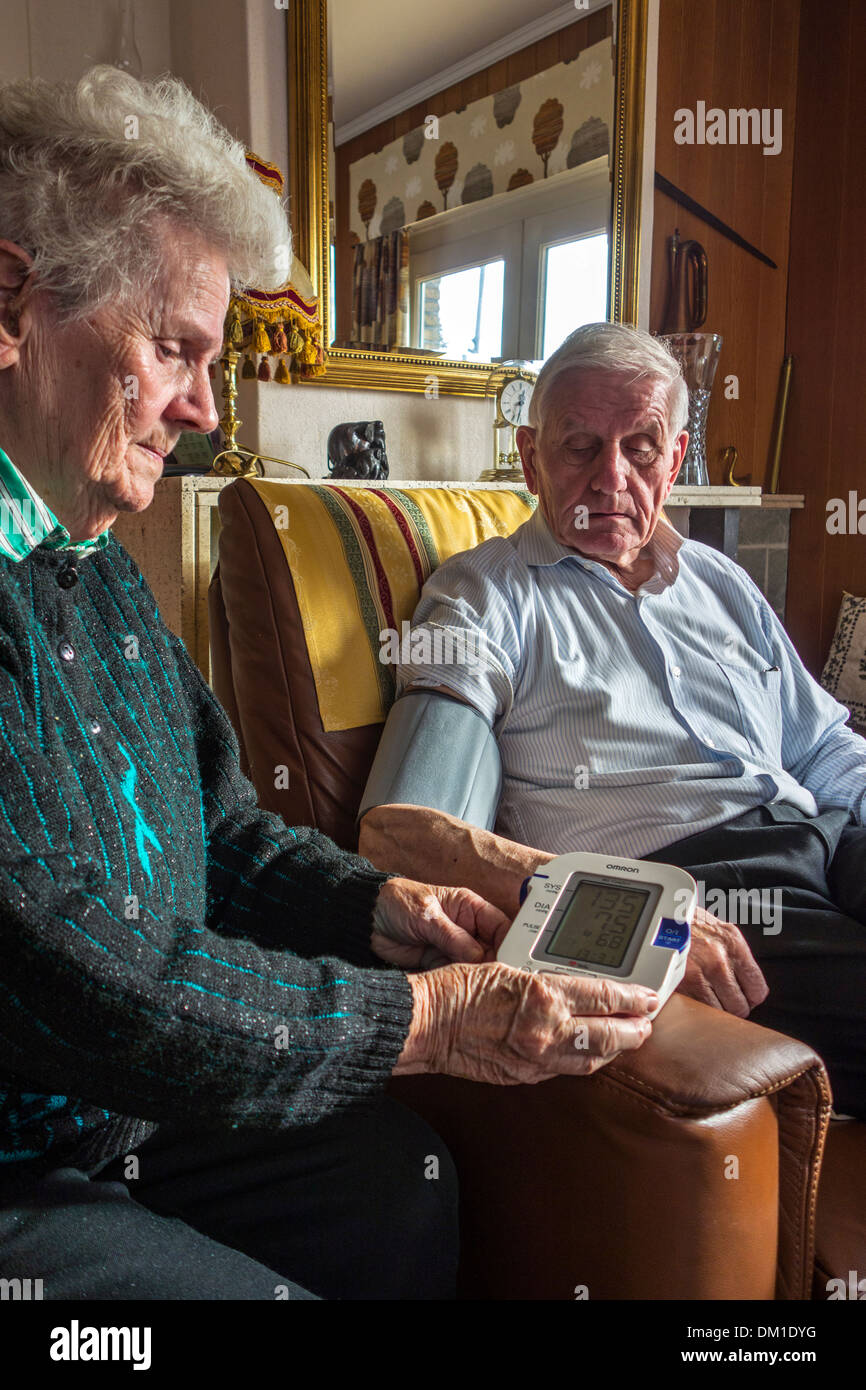 Nahaufnahme eines älteren Ehepaares, die Überprüfung ihrer eigenen Blutdrucks mit einem digitalen Blutdruckmessgerät im Wohnzimmer zu Hause Stockfoto