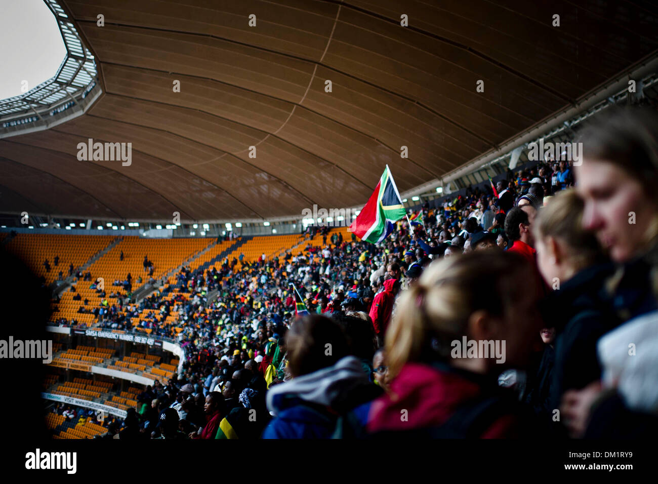 Johannesburg, Südafrika. 10. Dezember 2013. Tausende von Menschen versammelt, um die letzte Ehre, des verstorbenen ehemaligen südafrikanischen Präsidenten, Nelson Mandela, während der offiziellen National Memorial Service Zahlen auf das FNB-Stadion in Soweto, Johannesburg statt. Trauernde singen im Regen während der Feier. Foto: ImageSA/Alamy Live-Nachrichten Stockfoto