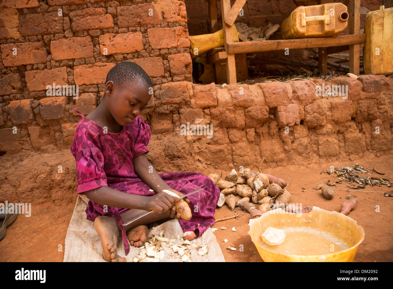 Ein Kind schält Kartoffeln vor ihrem Haus in Gombe, Uganda, Ostafrika. Stockfoto