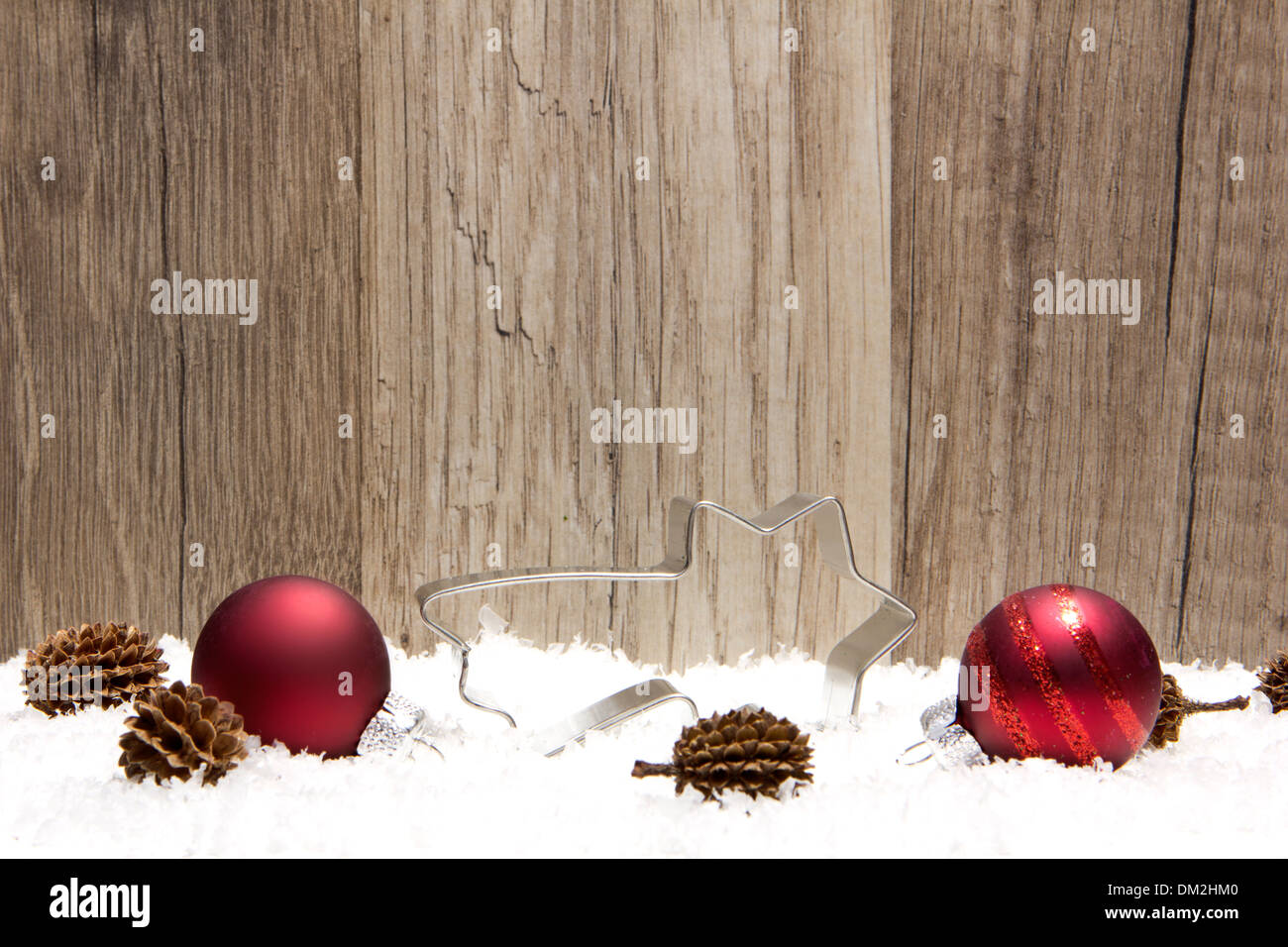 Weihnachts-Dekoration mit hölzernen Hintergrund, Schnee, Weihnachtskugeln rot, Shootingstar und Tannenzapfen Stockfoto