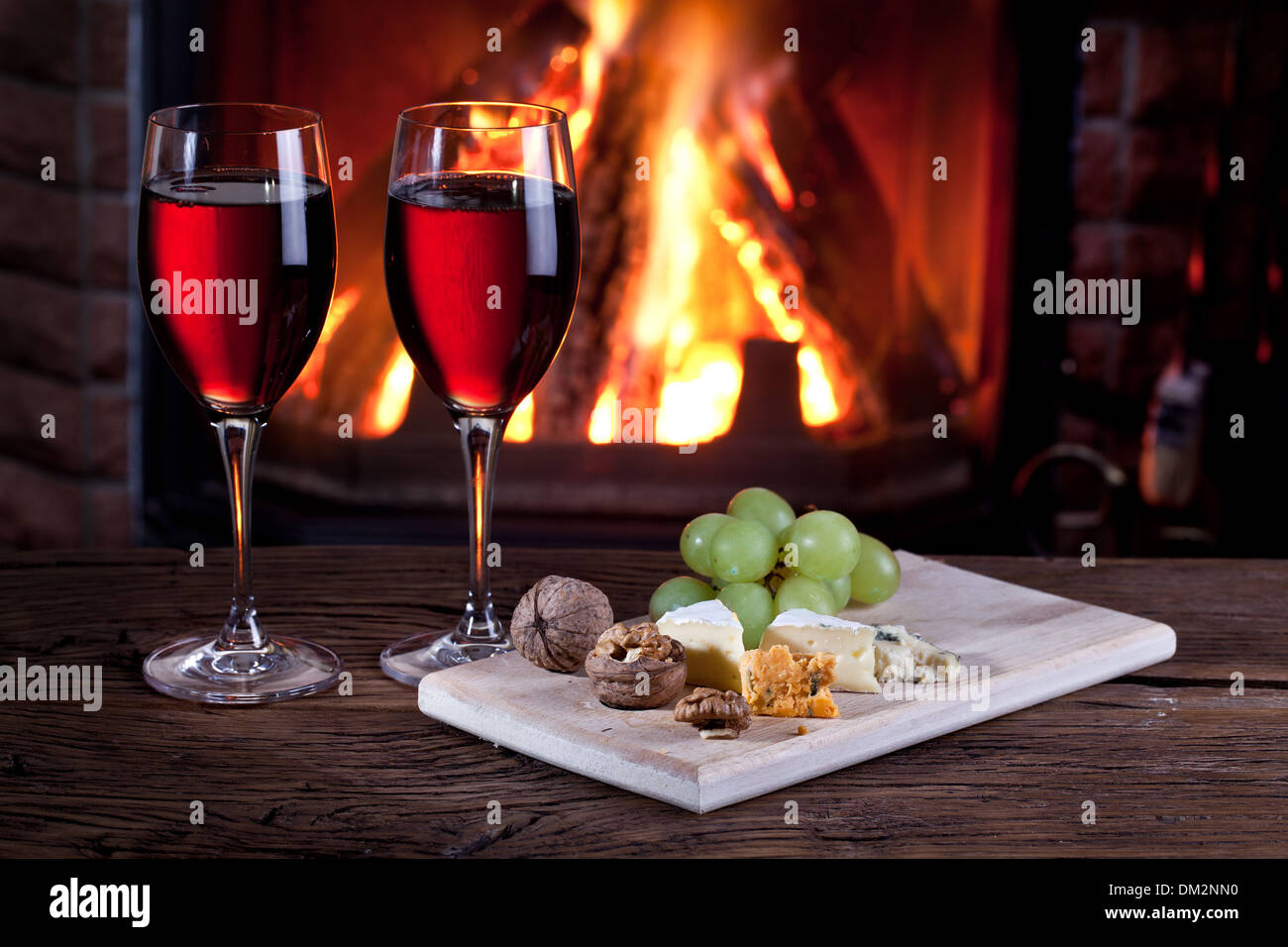 Romantisches Stilleben am Kamin. Gläser Wein, Käse und Nüssen. Stockfoto