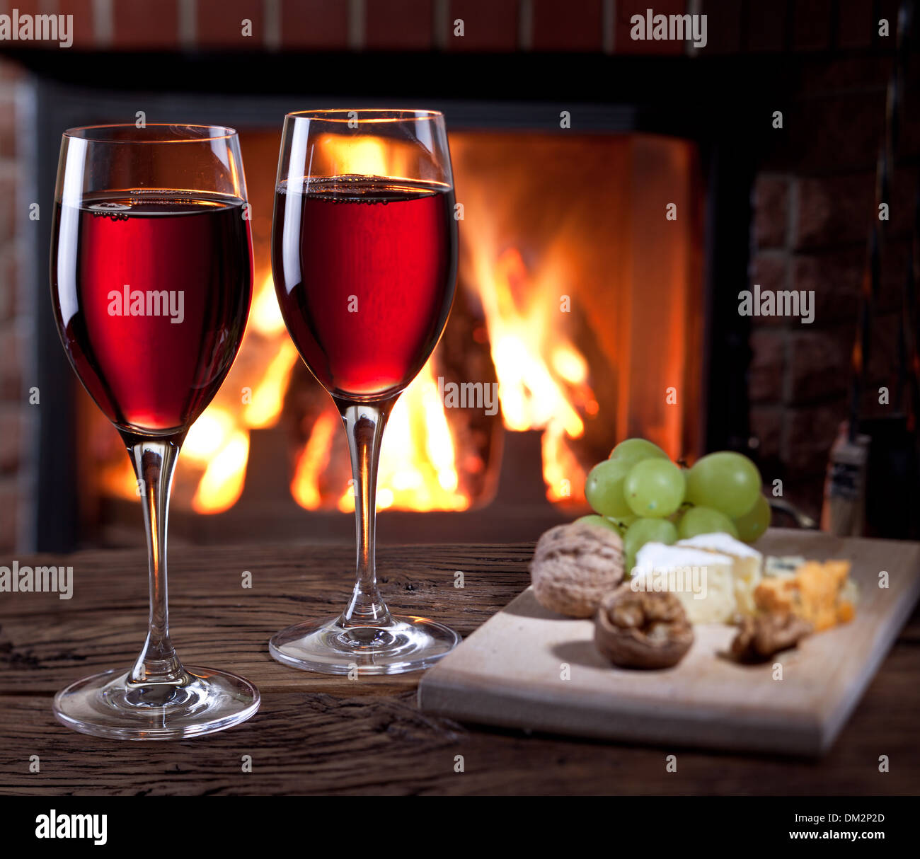Romantisches Stilleben am Kamin. Gläser Wein, Käse und Nüssen. Stockfoto