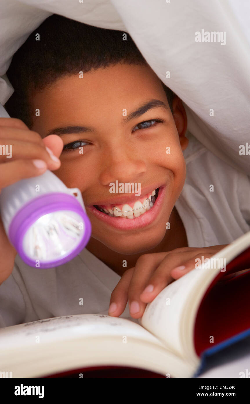 Junge Lesebuch mit Taschenlampe unter der Bettdecke Stockfoto