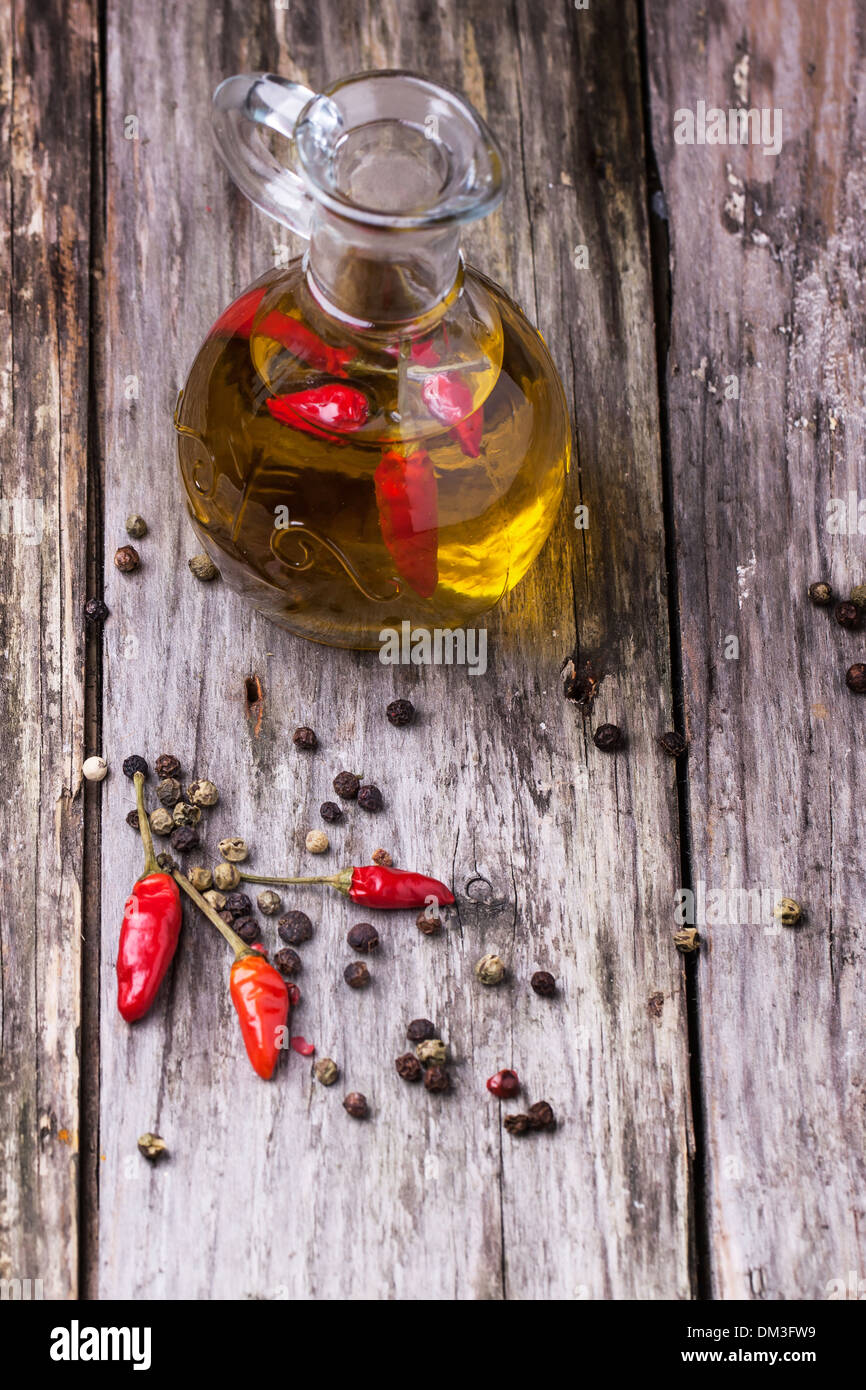 Glasflasche Olivenöl mit rote scharfe Chilischoten über alten hölzernen Hintergrund. Serien ansehen Stockfoto