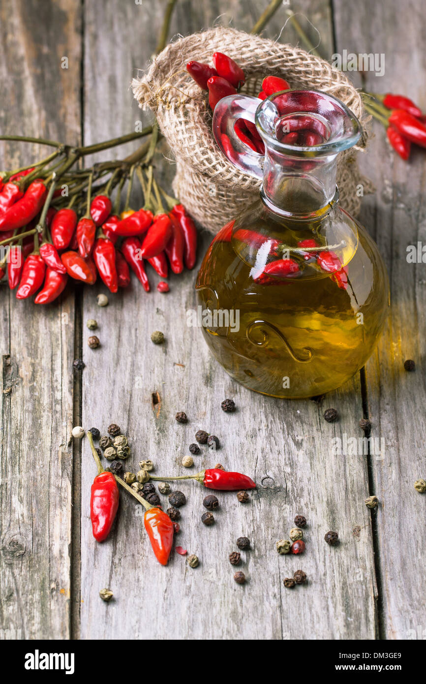 Glasflasche Olivenöl mit rote scharfe Chilischoten über alten hölzernen Hintergrund. Serien ansehen Stockfoto