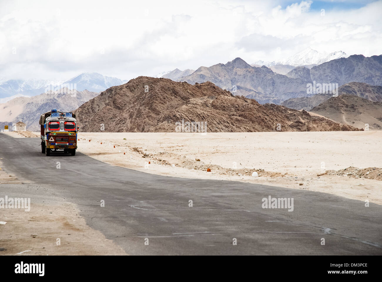 Ladakh, Indien - 13. Juli 2009: ein bunte LKW fährt auf einer abgelegenen Straße umgeben von hohen Bergen. Dramatische Wolken und Himmel. Stockfoto