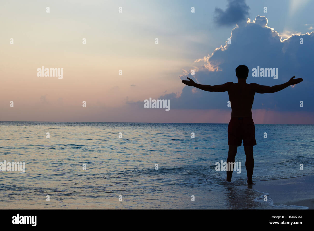 Silhouette der Mann mit ausgestreckten Armen am Strand bei Sonnenuntergang Stockfoto