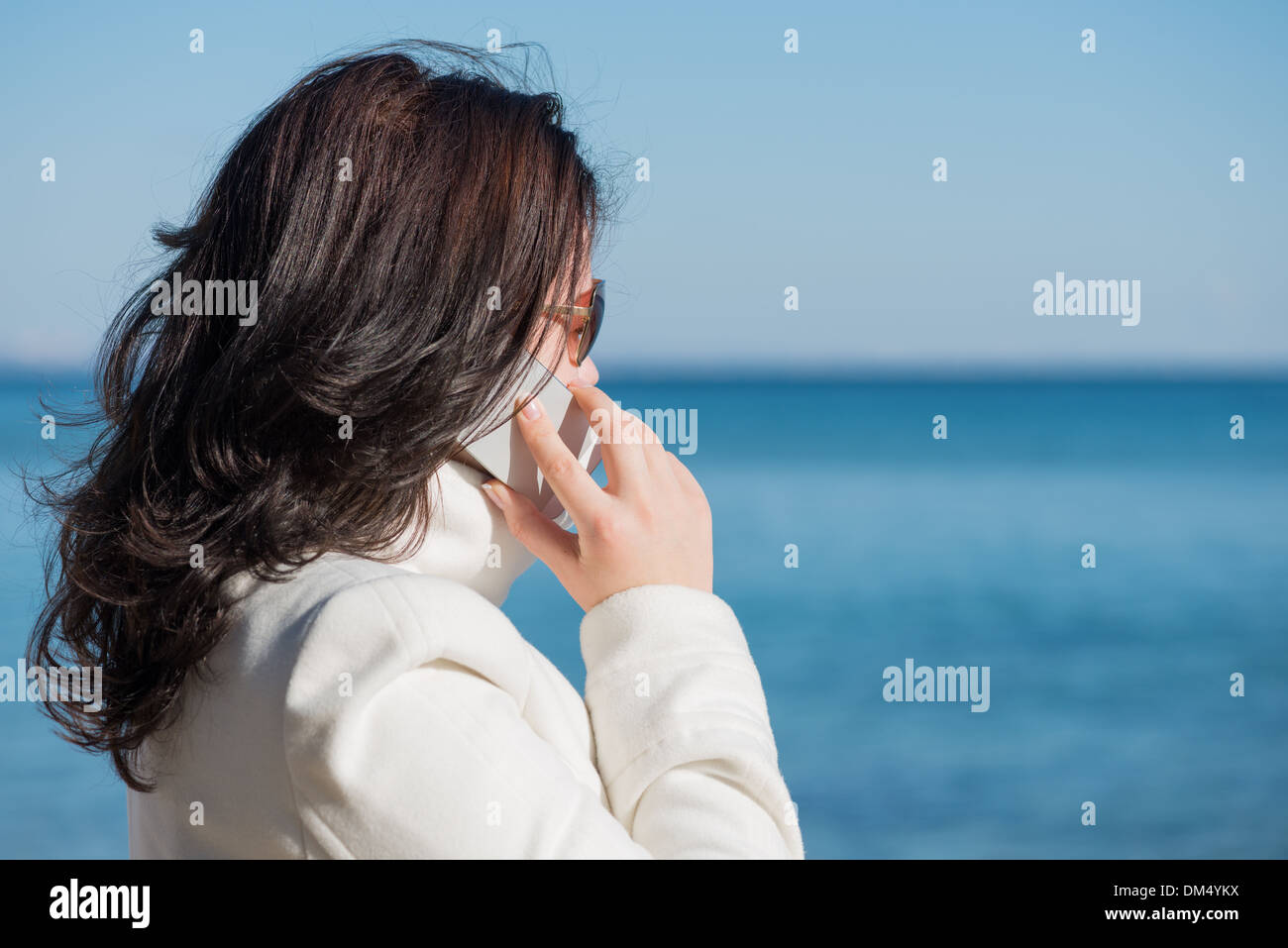 Junge Frau spricht mit dem Handy am Meer und mit Blick auf das Meer. Es ist Frühling. Stockfoto