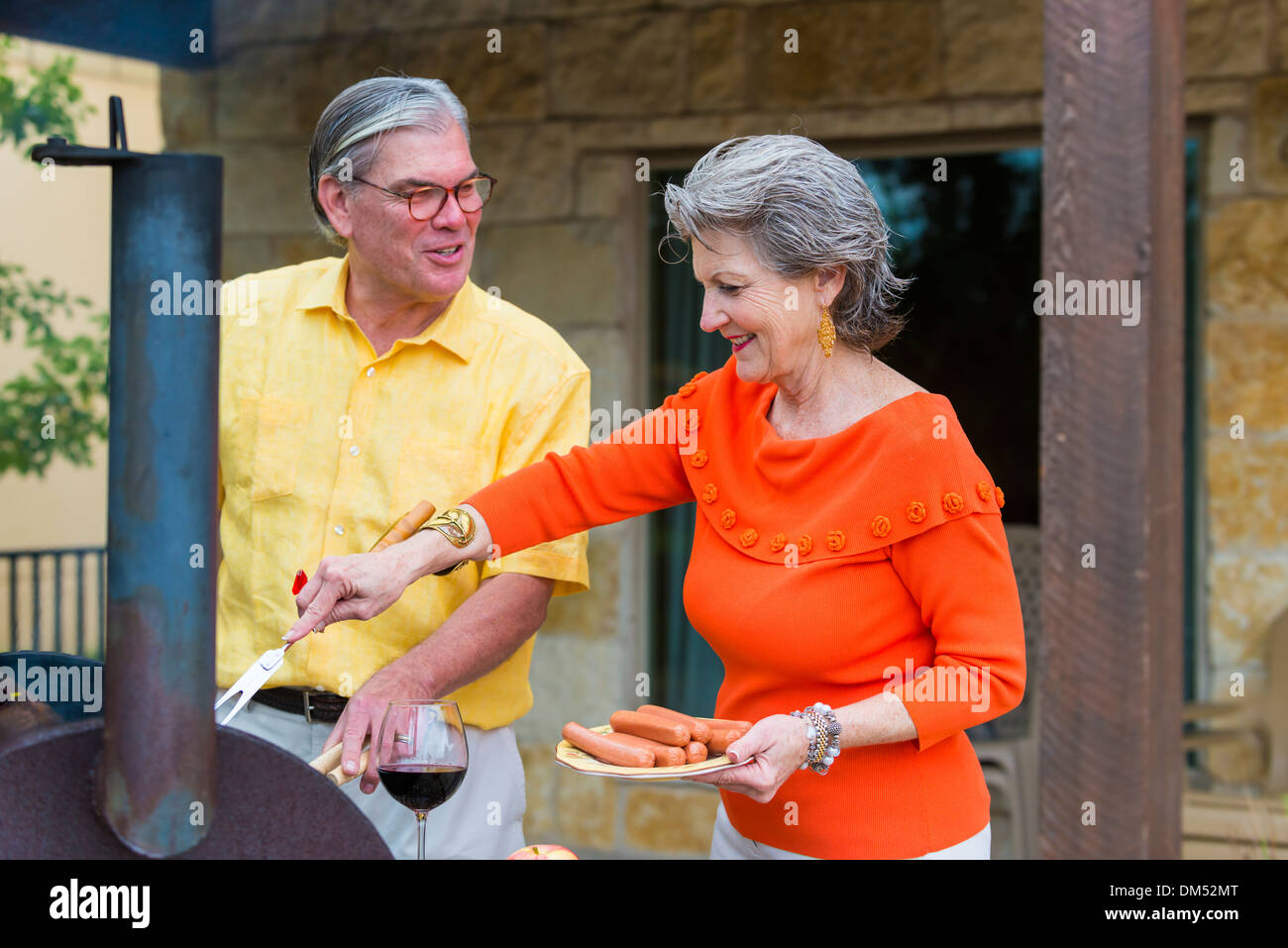 Älteres paar Vorbereitung ein Barbecue auf der Rückseite ihrer Heimat, Texas, USA. Frau setzt die Würstchen auf dem Grill. Stockfoto