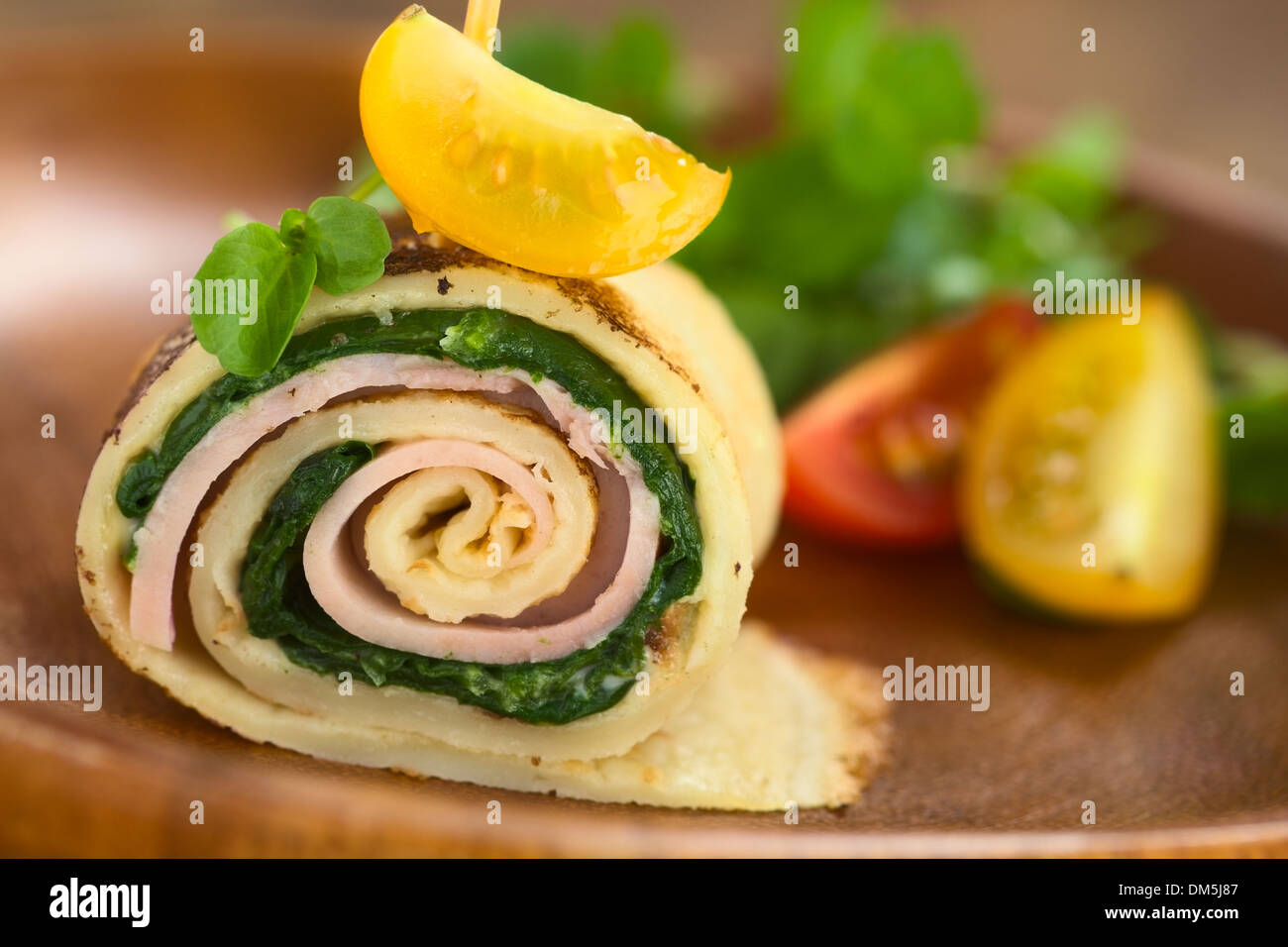 Crêpe-Roll als Fingerfood, gefüllt mit Spinat und Schinken garniert mit Kirschtomaten und Kresse auf Holzteller serviert Stockfoto