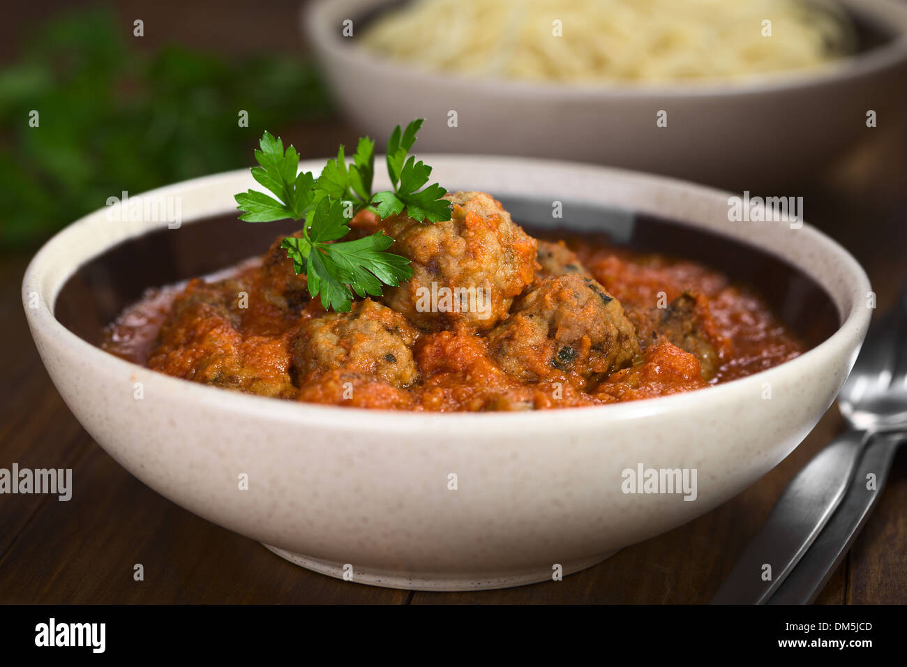 Spanische Albondigas (Fleischbällchen) in Tomatensoße in Schüssel geben, mit Petersilie garniert Stockfoto