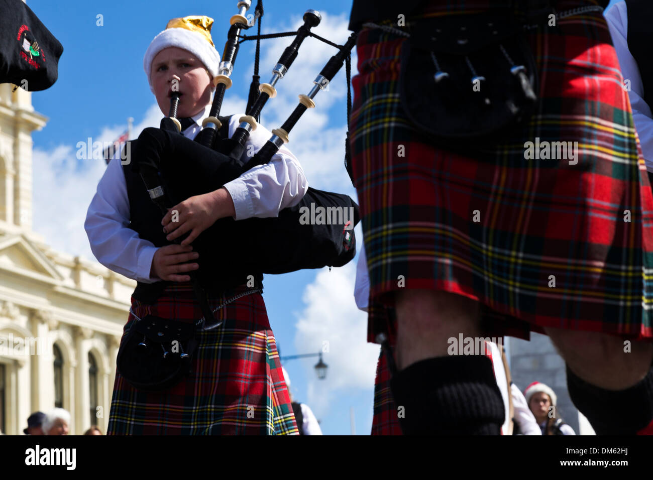Eine junge Piper in einer schottischen Band trägt eine Weihnachtsmütze während der jährlichen Christmas parade Stockfoto
