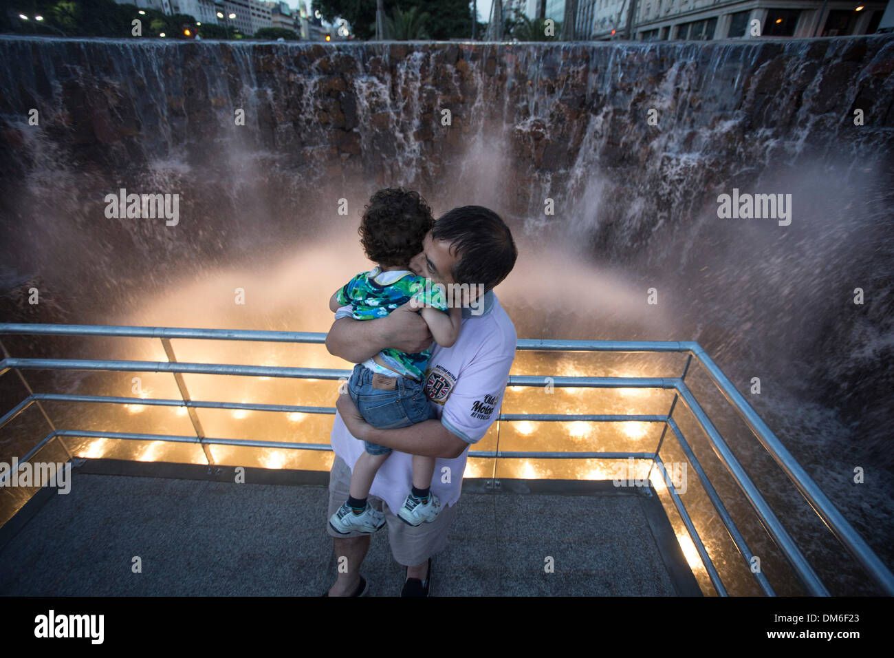 Buenos Aires, Argentinien. 12. Dezember 2013. Ein Mann hält seine Enkel steht vor eine verkleinerte Nachbildung des "La Garganta del Diablo", eines der berühmtesten springt die Iguazu-Wasserfälle an der Grenze Brasilien und Argentinien, am 9.Juli Ave in der Stadt Buenos Aires, Argentinien, 11. Dezember 2013. Das Replikat ist mit Steinen von den Iguazu Wasserfällen für die Förderung dieses Touristenziel gebaut. Bildnachweis: Martin Zabala/Xinhua/Alamy Live-Nachrichten Stockfoto