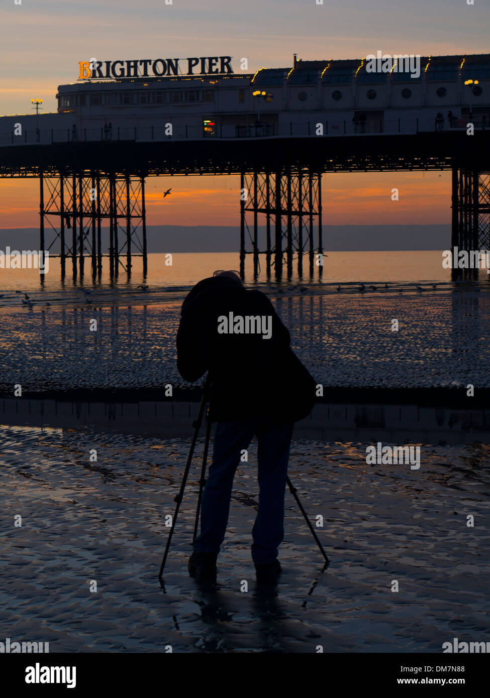 Ein Fotograf fängt Sonnenuntergang über Brighton Pier bei Ebbe Stockfoto