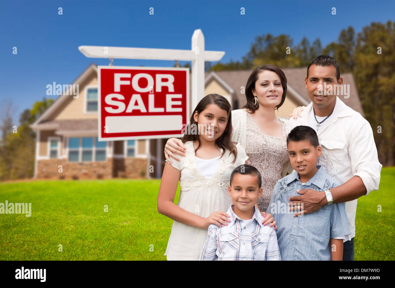 Junge glückliche hispanische junge Familie vor ihrem neuen Haus und Immobilien Verkaufsschild. Stockfoto