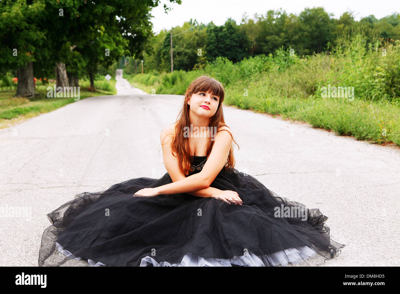 Porträt von Teenager-Mädchen sitzen im schwarzen Kleid auf einer Landstraße im ländlichen Indiana. Stockfoto