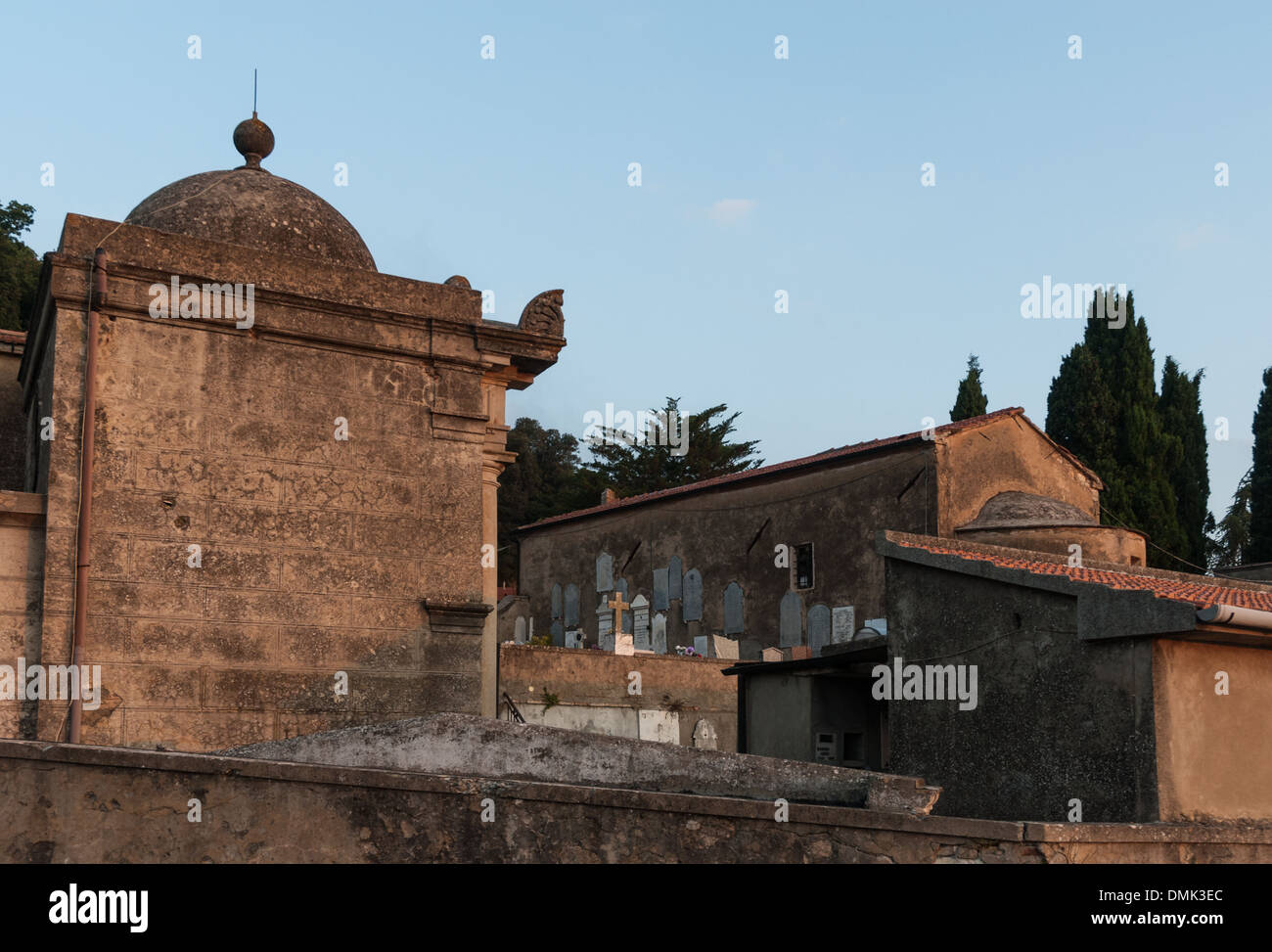 Der Friedhof Sassetta in Italien wird während des Sonnenaufgangs erfasst, wobei das sanfte Licht die Gräber und die umliegende Landschaft beleuchtet. Diese friedliche Umgebung spiegelt die ruhige Atmosphäre des Friedhofs bei Sonnenaufgang wider. Stockfoto