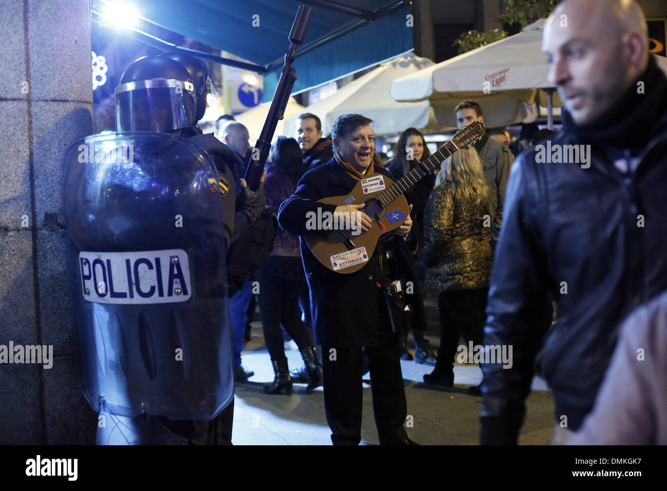 Madrid, Spanien. 14. Dezember 2013. Ein Mann spielt Gitarre, während die Polizei die Straße Afte Unruhen Rnear Parlament in Madrid, Samstag, 14. Dezember 2013 deutlich. Demonstranten, wütend auf Gesetzesvorhaben, das Ziel ist die schwere Strafen für Straftaten wie verursacht schwerwiegende Störungen außerhalb des Parlaments, versammelten sich in der Nähe von Spaniens Gesetzgeber unter den Augen eine starke Polizeipräsenz. Die Protestopposes die Einführung einer Gesetzesvorlage, die Geldbußen von bis zu 30.000 Euro ($40.800) für Straftaten wie brennen die Nationalflagge und insultin Kredit festgelegt werden: ZUMA Press, Inc./Alamy Live News Stockfoto