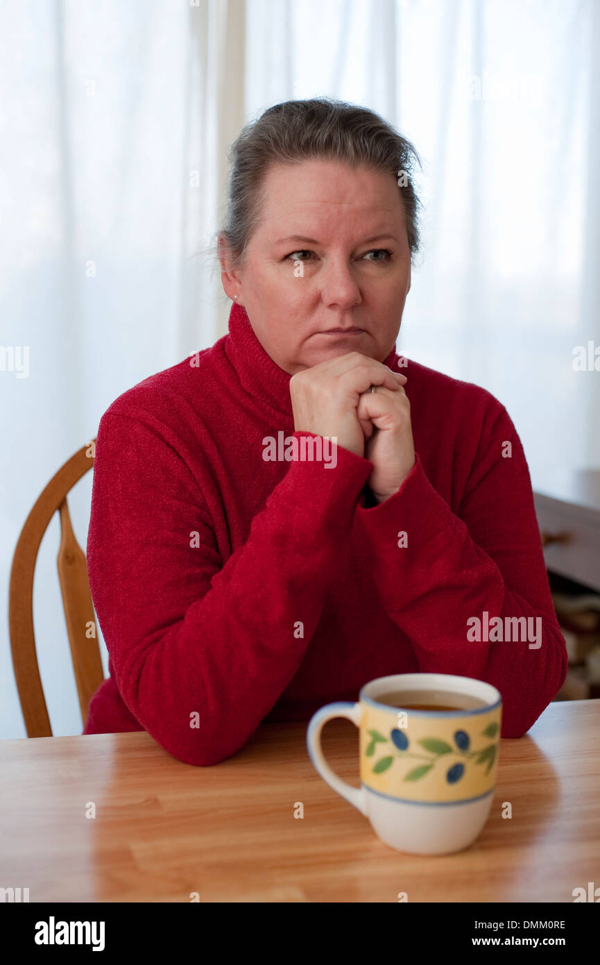 Reife Frau sitzt am Esstisch mit Tee mit besorgten Blick auf Gesicht widerspiegelt Stockfoto