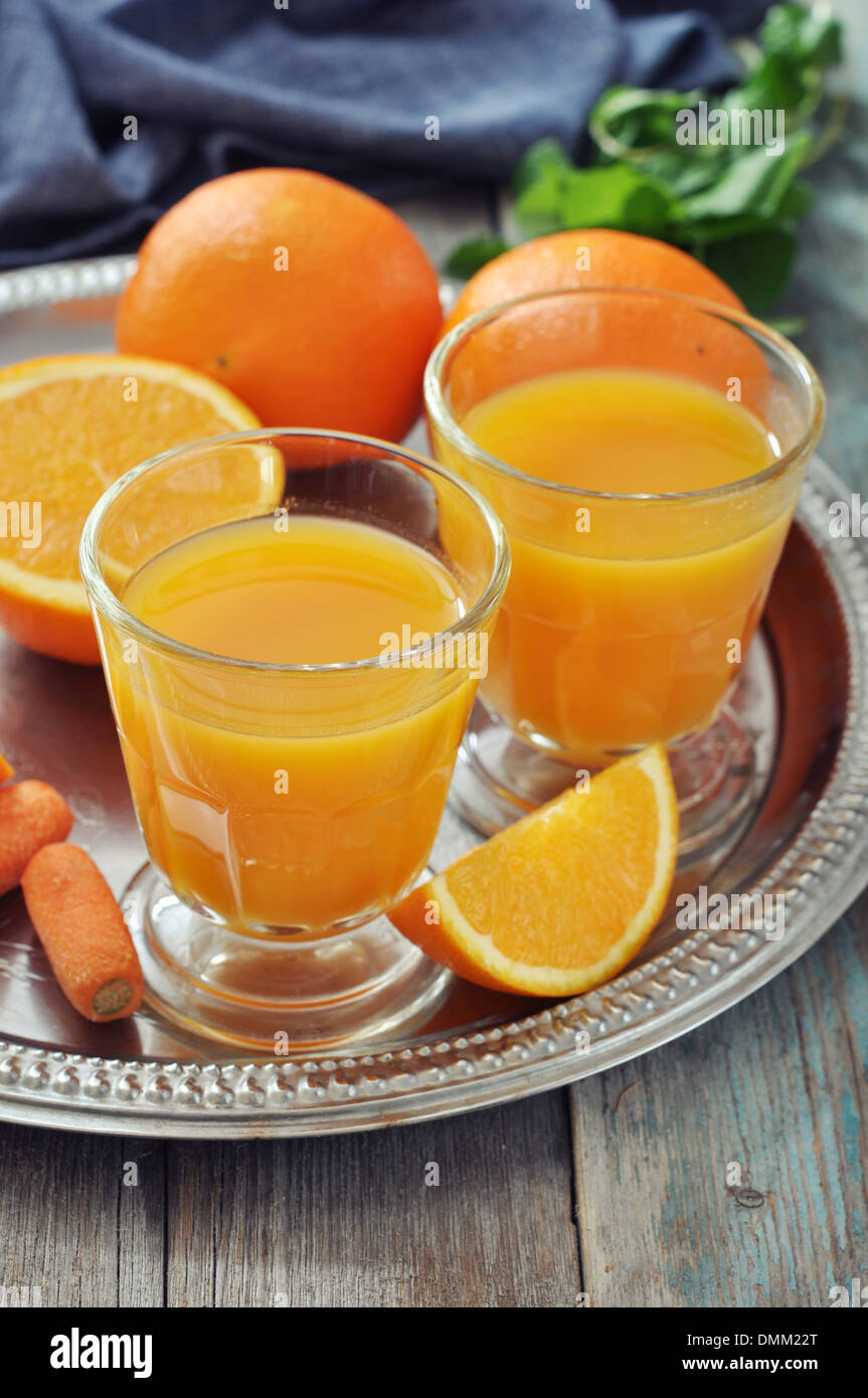 Orange und Karotten-Saft im Glas mit Minze, frisches Obst und Gemüse auf rundes Tablett Stockfoto